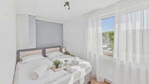 Et moderne soveværelse med seng, natborde, et vindue med let gardin og udsigt til grønne områder.
