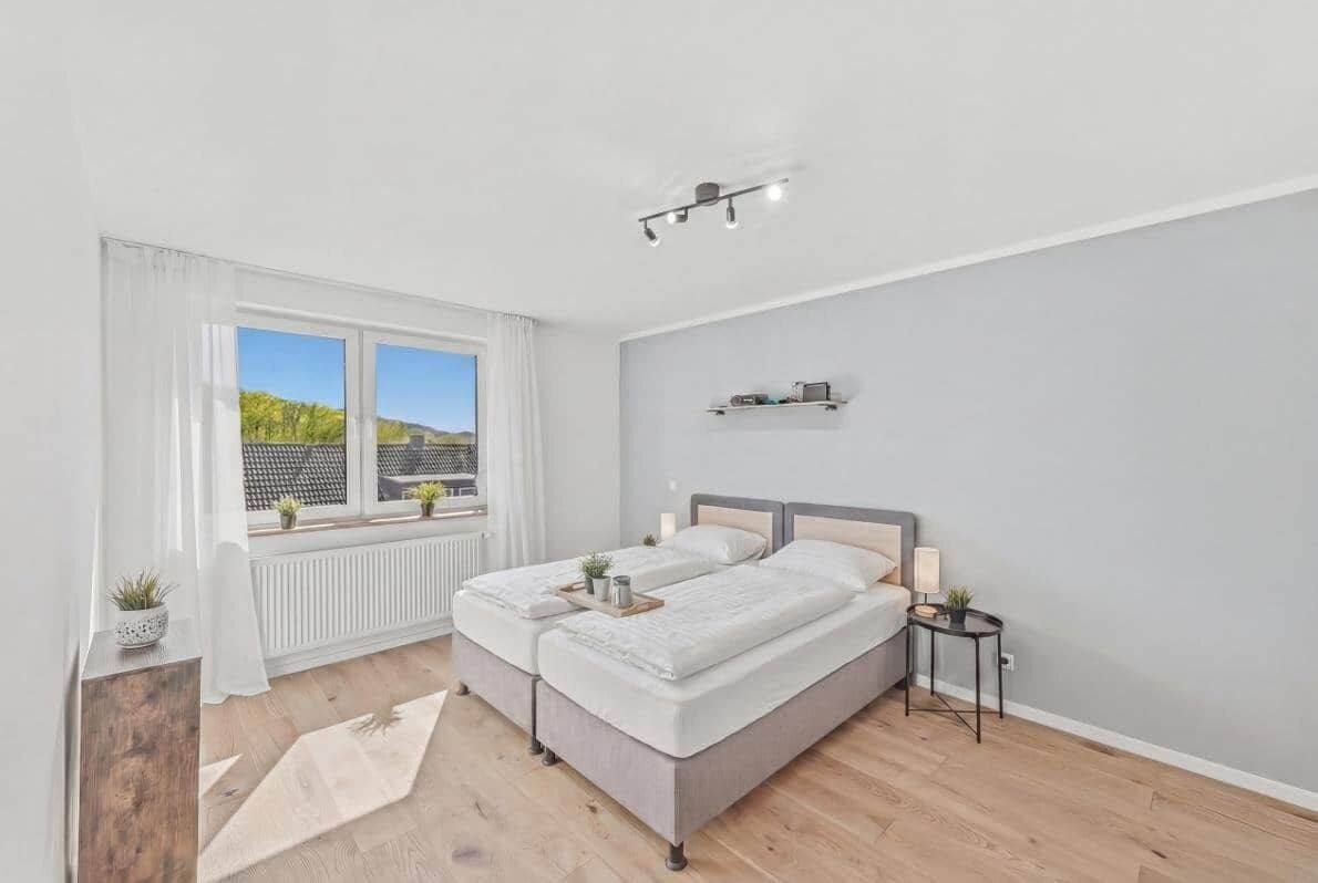 Ein Schlafzimmer mit zwei Betten, einem Fenster mit Blick, einem Nachttisch und einer Heizung.