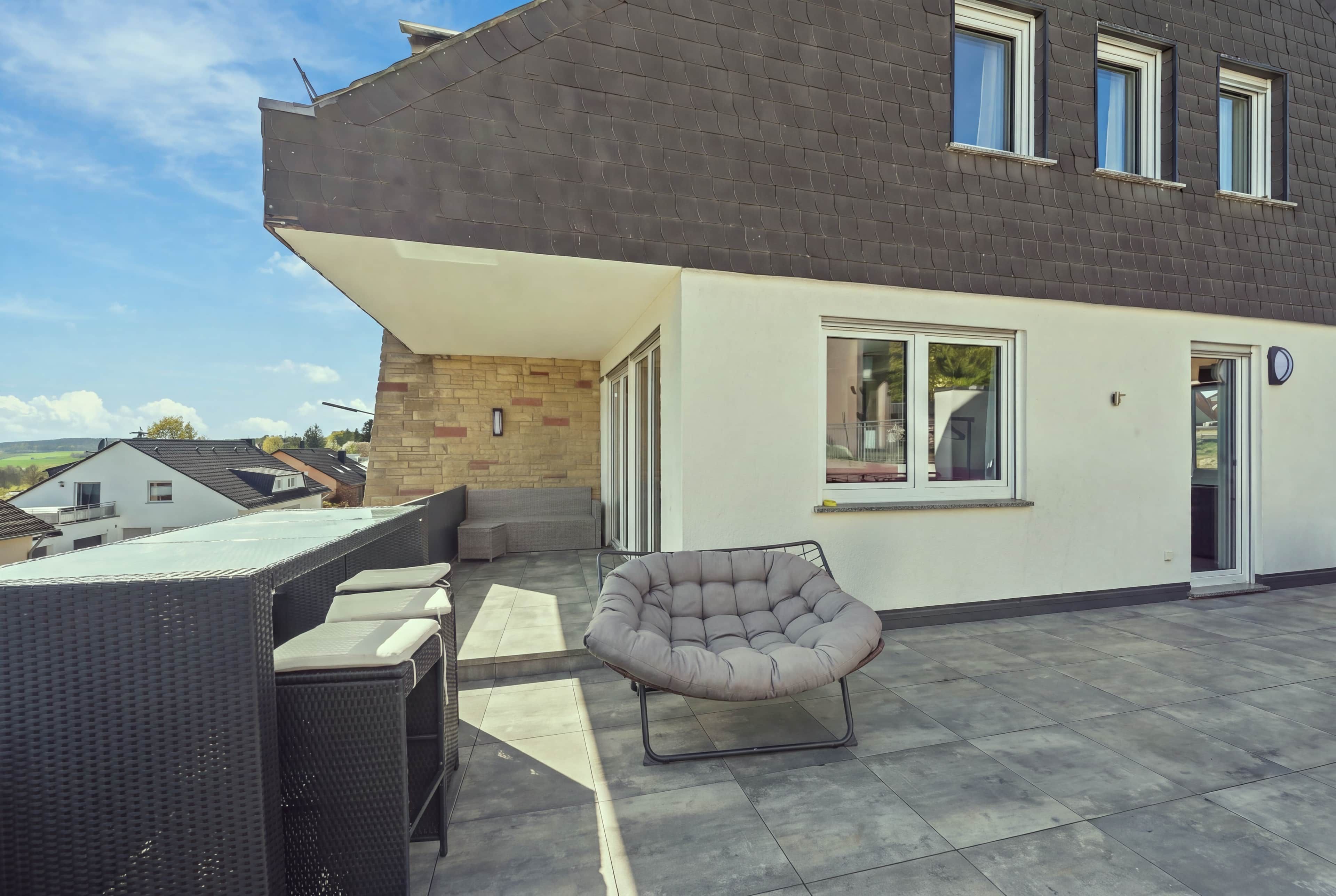 Un patio moderno con zona de estar, que incluye una silla acolchada y una mesa con sillas.