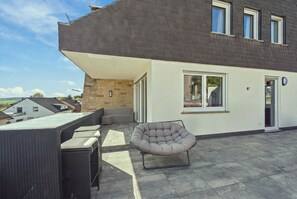 A modern patio with a seating area, including a cushioned chair and a table with chairs. - 15-minute walk | Accessible · 60m² balcony & cinema (Trierweiler)