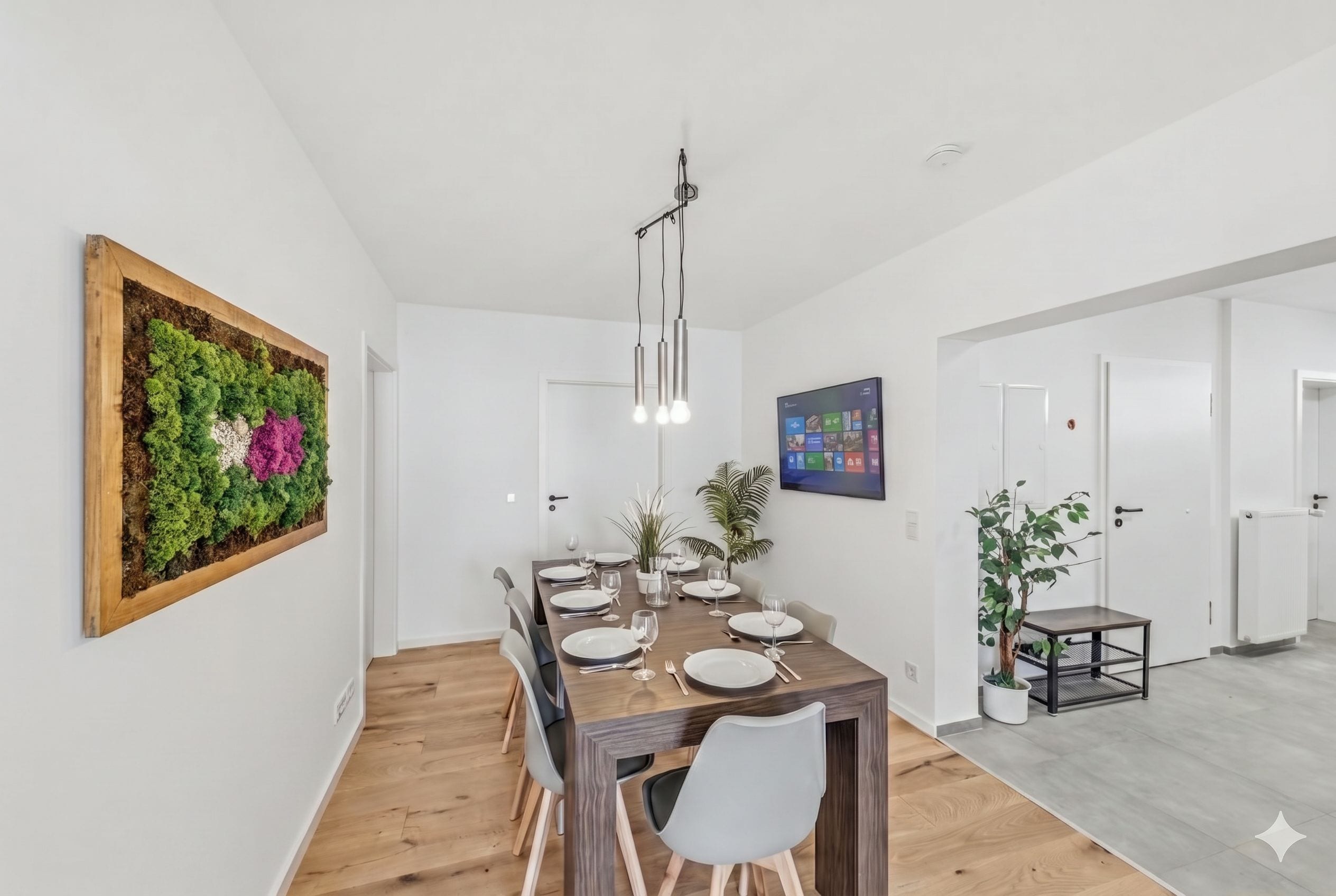 A dining area with a wooden table set for four, surrounded by chairs, with a hanging light fixture above.