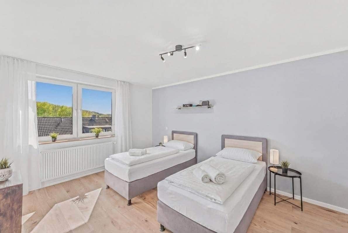 Slaapkamer met twee bedden, een raam met uitzicht, een radiator en een klein tafeltje met een lamp.