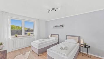 Slaapkamer met twee bedden, een raam met uitzicht, een radiator en een klein tafeltje met een lamp.