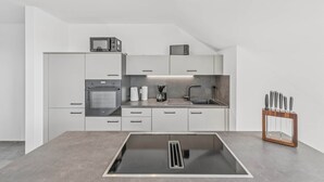 Una cocina moderna con armarios blancos, horno empotrado, cafetera y bloque para cuchillos.