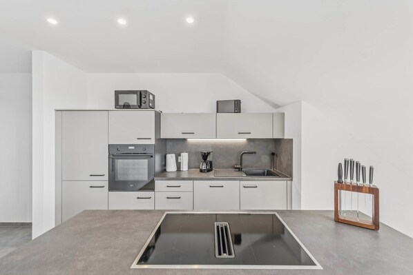 A modern kitchen with white cabinets, a built-in oven, a coffee maker, and a knife block.