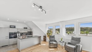 Cocina moderna con una isla central, sillas tapizadas en gris y amplias ventanas con vistas al exterior.
