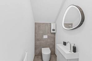 Un baño moderno con inodoro, lavamanos con espejo y dispensador de jabón.