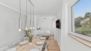 Un comedor moderno con una mesa de madera alargada dispuesta para seis comensales, un televisor en la pared y una ventana con vistas a zonas verdes.