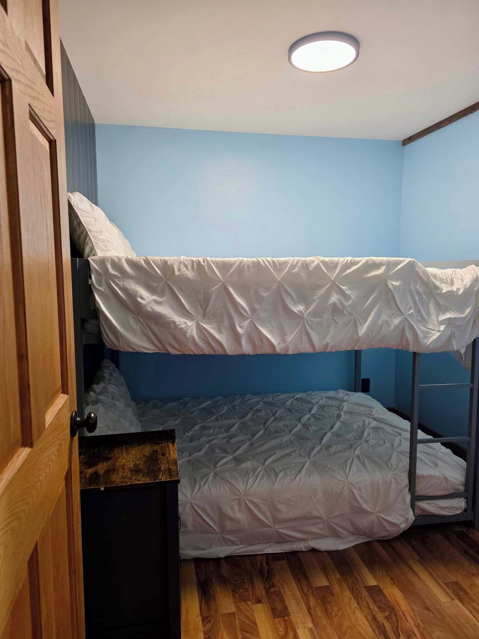 Een slaapkamer met stapelbedden, een houten deur, een plafondlamp en een blauwe wand.