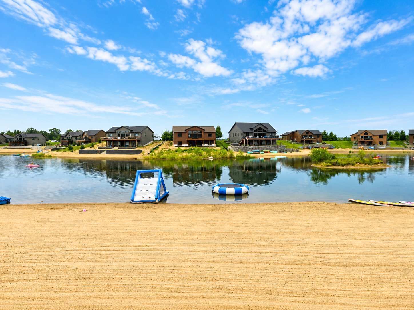 Blick auf einen See mit Häusern und einem Sandstrand.