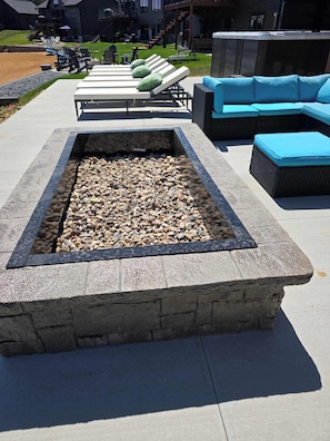 A stone fire pit surrounded by lounge chairs and a blue sofa.