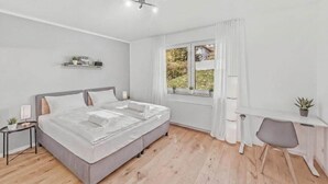 Un dormitorio moderno con cama, mesita de noche, silla, escritorio y ventana con cortinas.