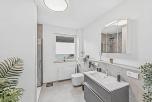 Un baño moderno con un espejo grande, una bañera, un inodoro y una ventana.