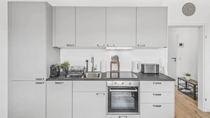 Una cocina moderna con armarios blancos, un lavamanos de acero inoxidable, horno empotrado y microondas.