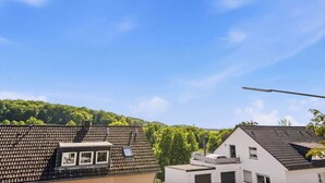 Una zona residencial con cielo azul despejado, una farola y una colina con vegetación al fondo.