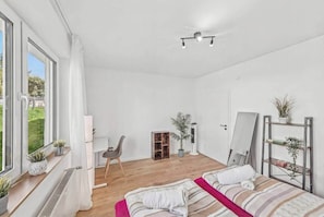 Un dormitorio con cama, escritorio, silla, espejo y radiador.