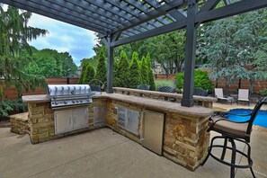 Cocina exterior con una parrilla, refrigerador y encimera de piedra.