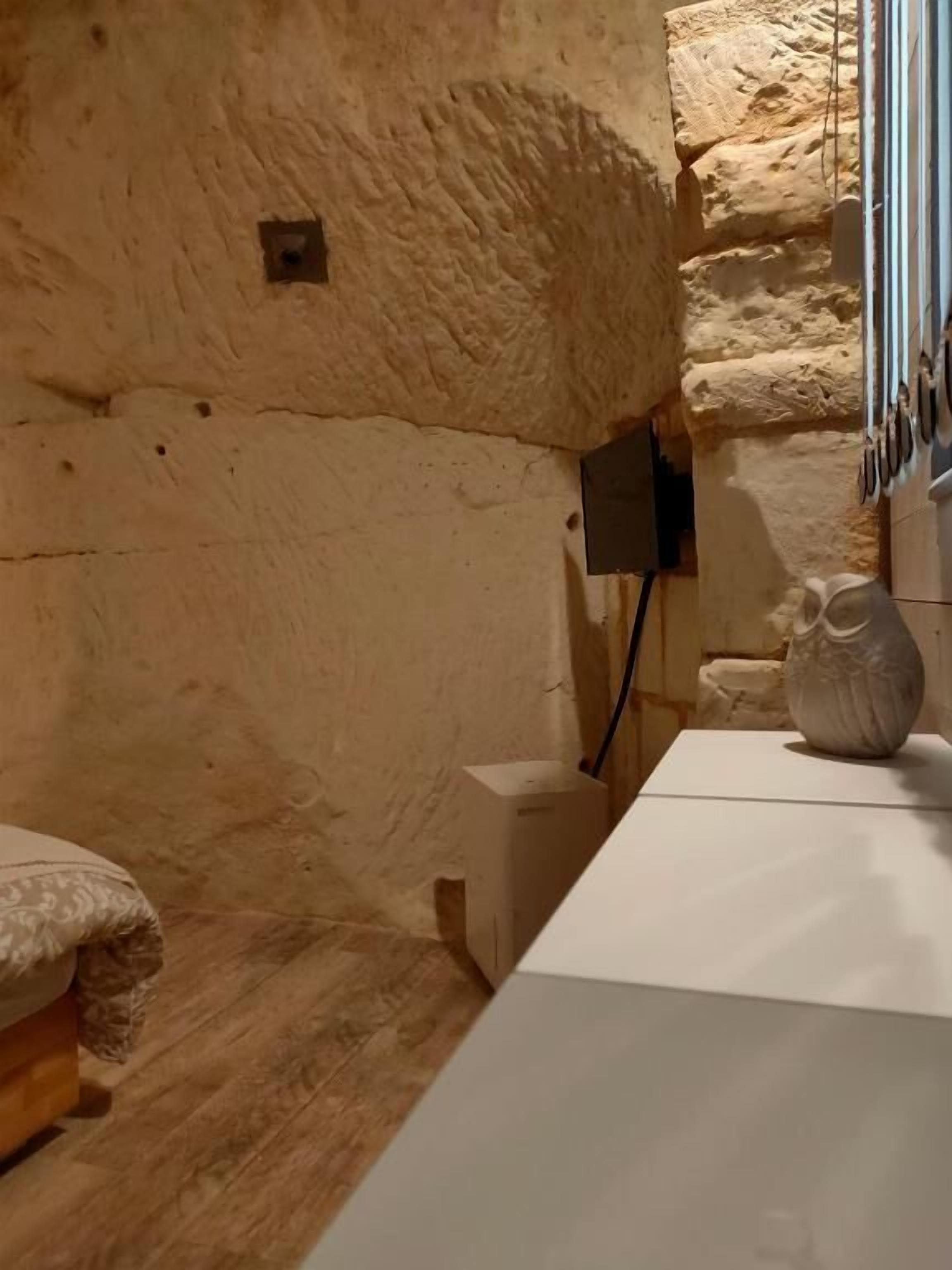 A room with a stone wall, a wooden floor, a white table, and a vase.