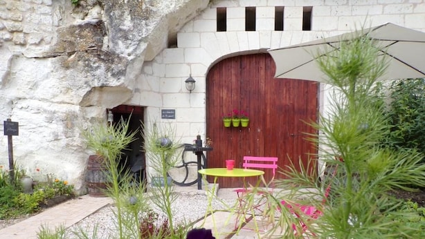 Un edificio rústico de piedra con una puerta de madera, una bicicleta, un banco rosa y una mesa amarilla.