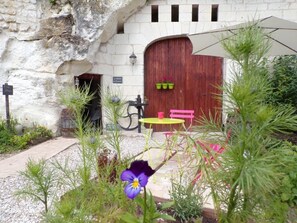 Un edificio rústico de piedra con una puerta de madera, una bicicleta, un banco rosa y una mesa amarilla.