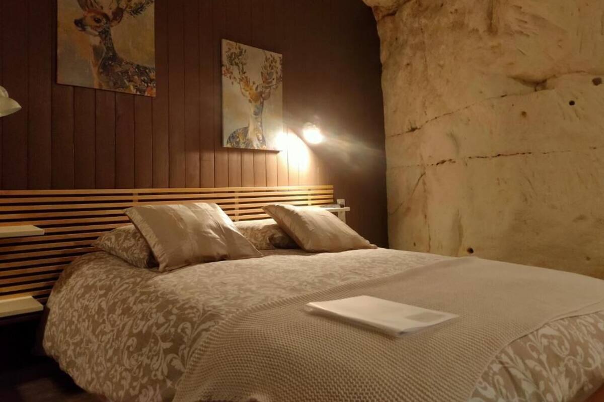 Un dormitorio con cabecera de madera, cama con ropa de cama estampada, dos lámparas de pared y dos cuadros.