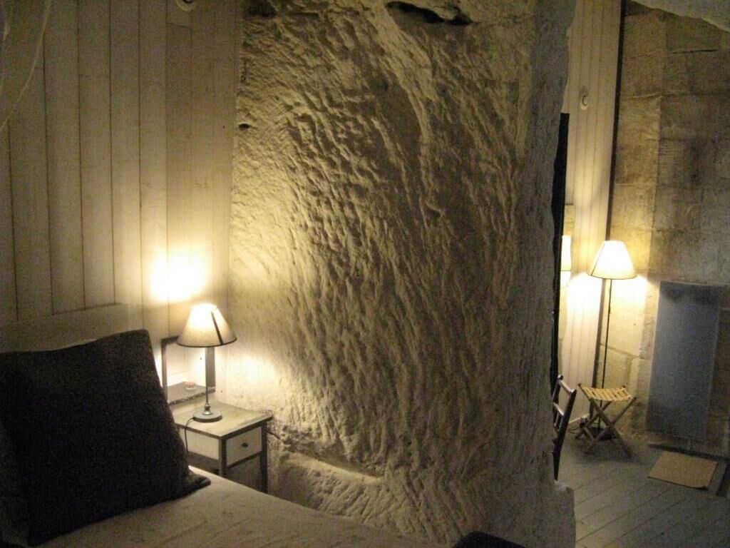 A room with a stone wall, a bed with a pillow, a nightstand with a lamp, and a chair.