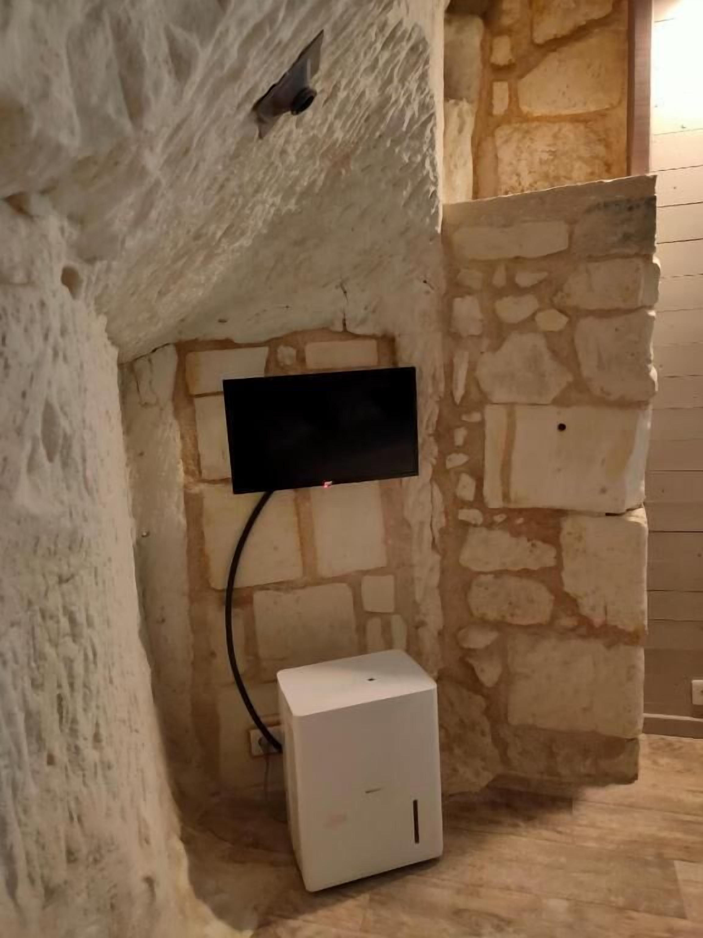 Une pièce avec un mur en pierre, un téléviseur à écran plat fixé au mur et une boîte électrique blanche.