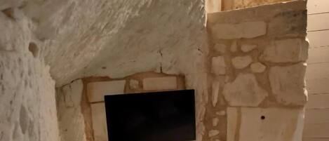 Une pièce avec un mur en pierre, un téléviseur à écran plat fixé au mur et une boîte électrique blanche.