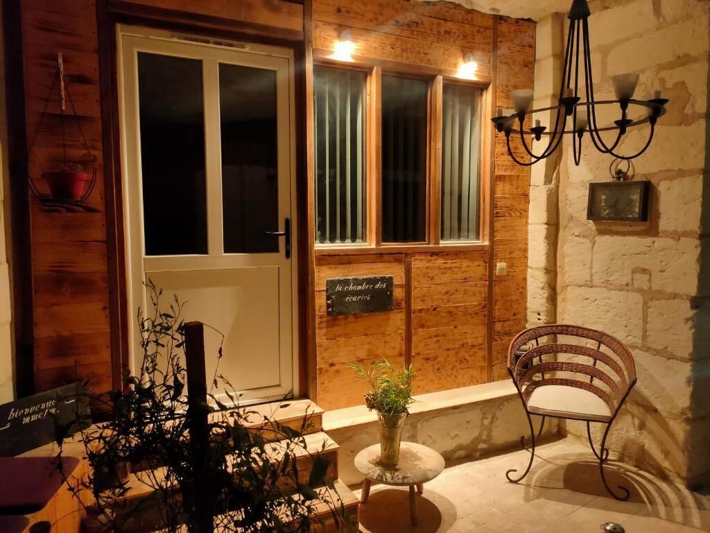 A wooden exterior wall, a door, a bench, a small table with a plant, and a sign.