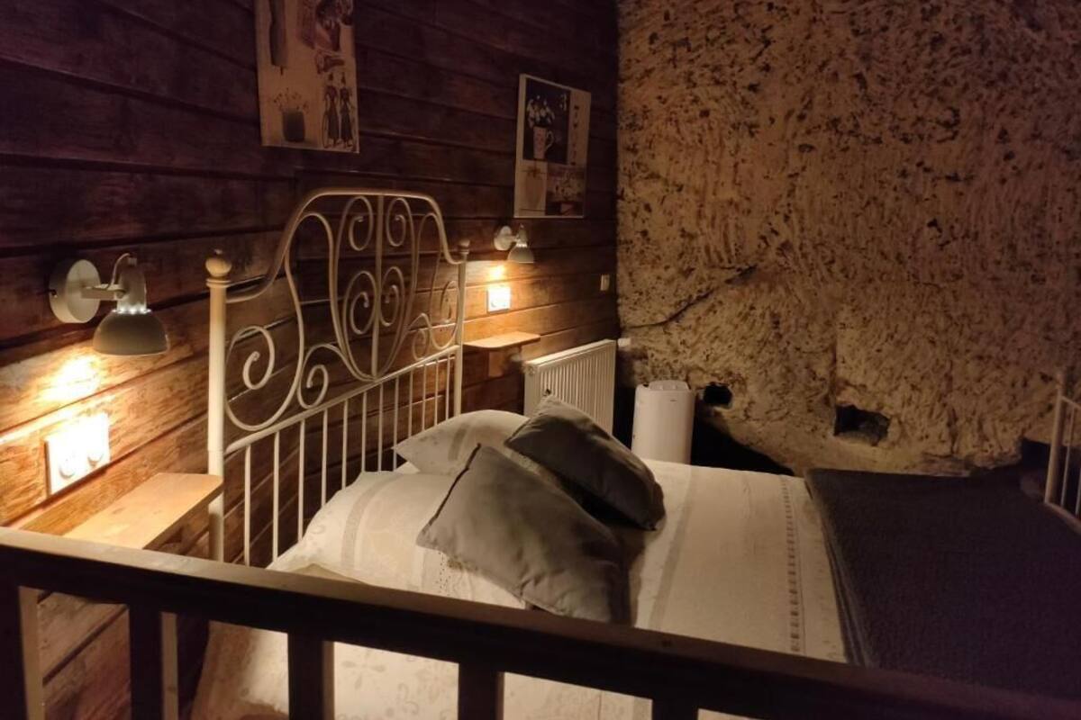 Habitación rústica con cabecera de madera, cama con almohadas, mesita de noche con lámpara y radiador.