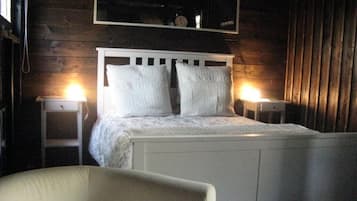 A bed with white bedding, two bedside tables with lamps, a chair, and a wooden wall with a mirror above the bed.