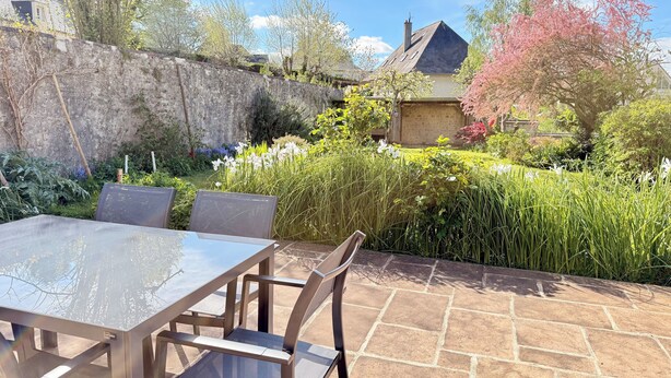 Eine Terrasse mit Tisch und Stühlen, umgeben von einer Steinsäule und üppiger Bepflanzung.