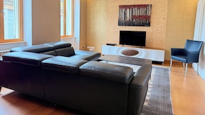 Ein modernes Wohnzimmer mit einem Ecksofa, einem Flachbildfernseher, einem weißen Konsolentisch und einem blauen Sessel.