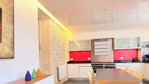 Eine moderne Küche mit weißen Schränken, einer roten Spritzschutzwand und einem Essbereich mit Holztisch und Stühlen.
