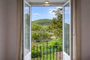 Une pièce dotée d’une grande fenêtre donnant sur un paysage vallonné, avec de la verdure et un bâtiment situé au loin.
