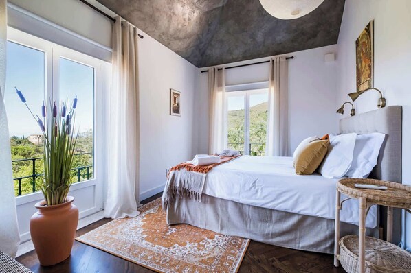 Une chambre à coucher avec un lit, une plante en pot, une fenêtre et une vue sur la verdure.