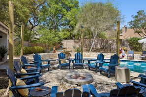 Un patio al aire libre con sillas Adirondack, una chimenea y una piscina.
