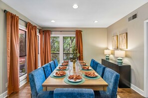 Comedor con una larga mesa dispuesta para seis, sillas tapizadas en azul y vistas a árboles a través de amplios ventanales.