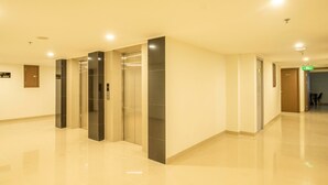 Um corredor moderno de hotel com elevadores, uma receção e uma placa a indicar os números dos quartos.