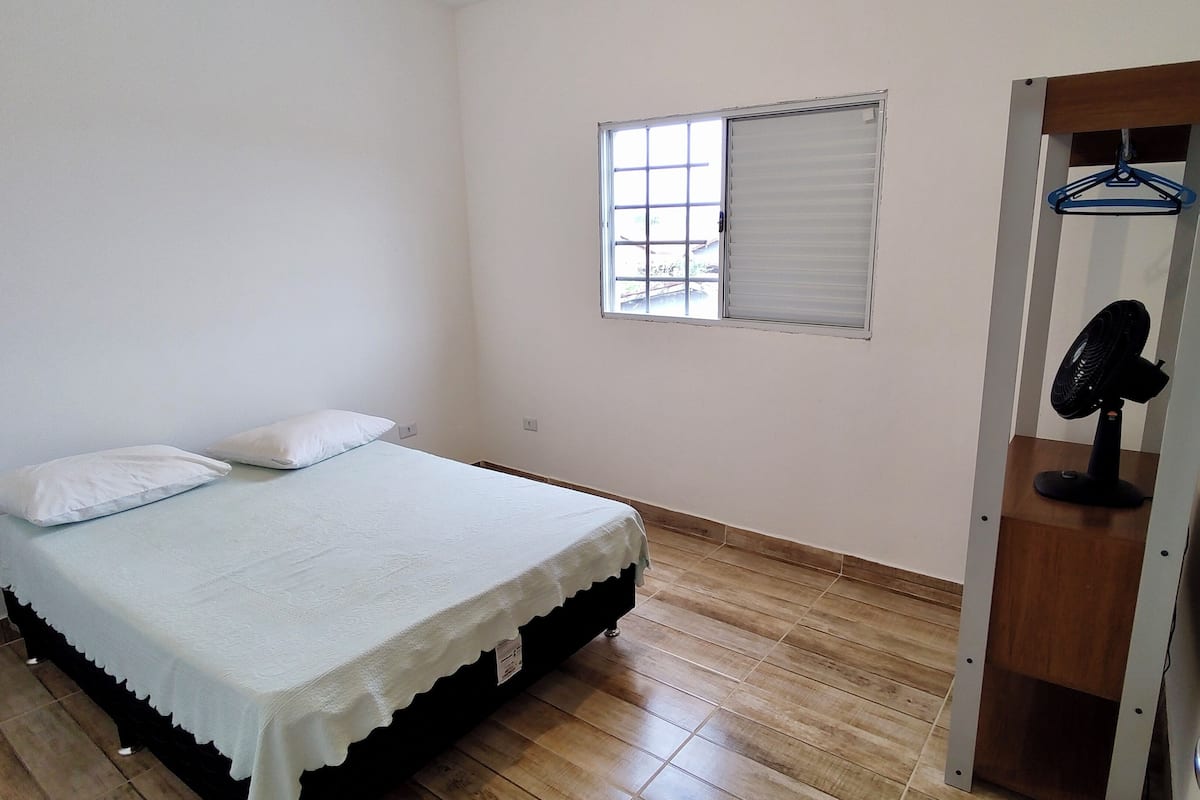 A bedroom with a bed, a window, a door with a fan, and a wooden floor.