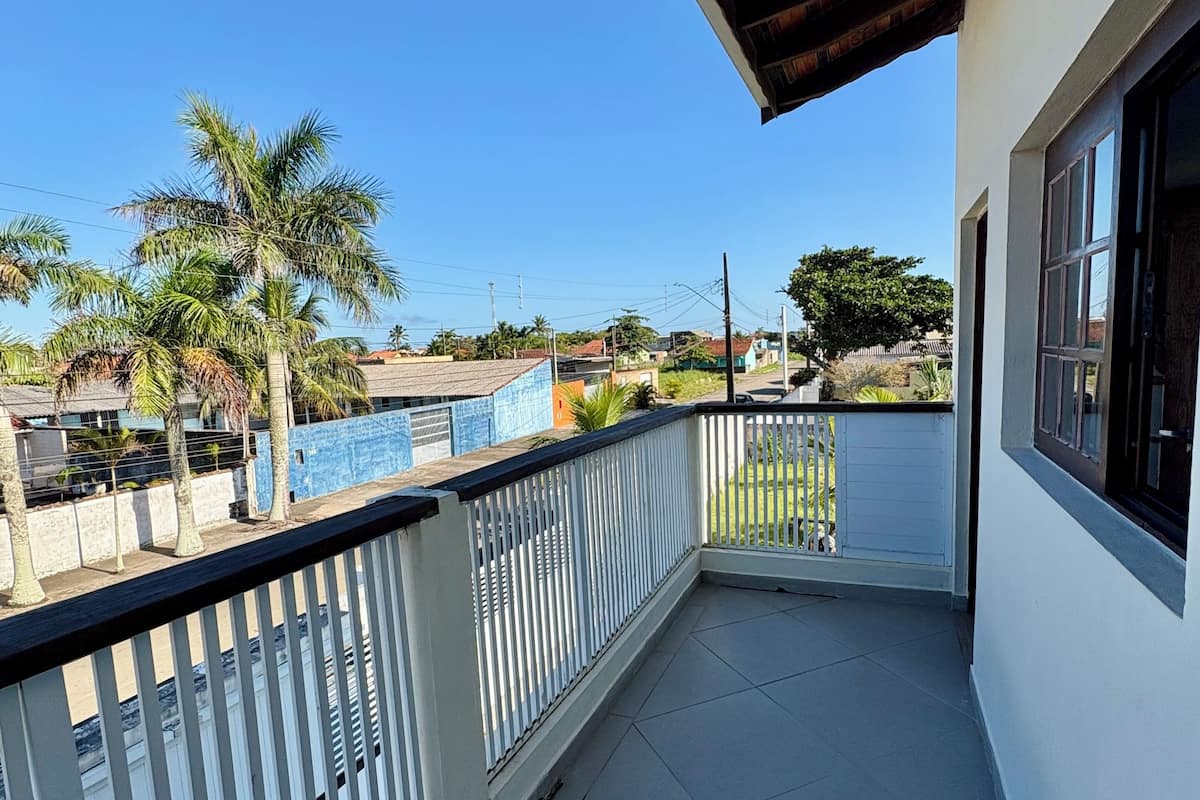 A balcony with a view of a swimming pool, palm trees, and a clear sky.