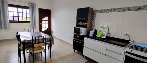 Een keuken met een eettafel, stoelen, een magnetron, een spoelbak en een fornuis.