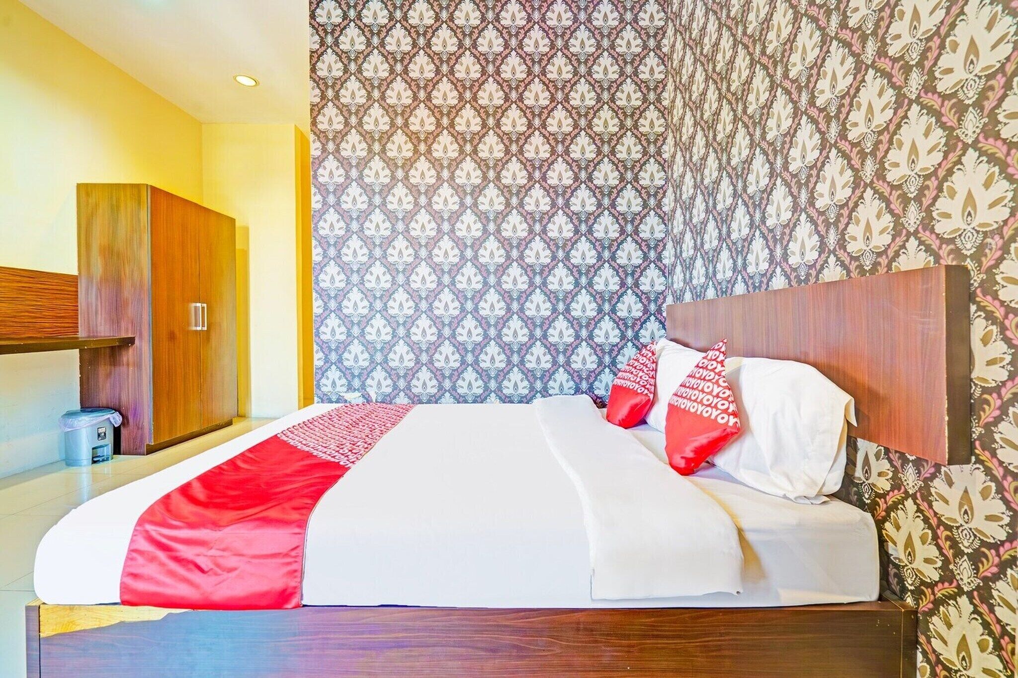 A hotel room with a bed, a wardrobe, and patterned wallpaper.