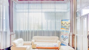 Een kamer met een groot raam, een bank, een kleine tafel en een poster aan de muur.