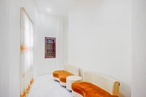Une pièce avec un mur blanc, une fenêtre ornée d’un cadre décoratif et deux canapés avec des coussins orange.