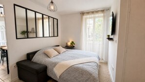 Un dormitorio con cama, mesita de noche, lámpara y televisor montado en la pared.