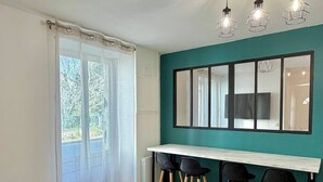 Un comedor con mesa de madera y sillas negras, pared de acento color aguamarina y un ventanal con vistas a árboles.