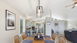 Eine moderne Küche mit weißen Schränken, ein Essbereich mit Holztisch und Stühlen sowie ein Wohnbereich mit Sofa und Fernseher.
