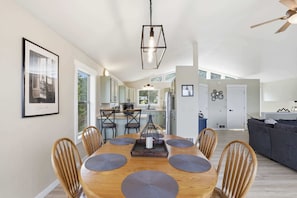 A modern kitchen with white cabinets, a dining area with a wooden table and chairs, and a living area with a sofa and a TV.