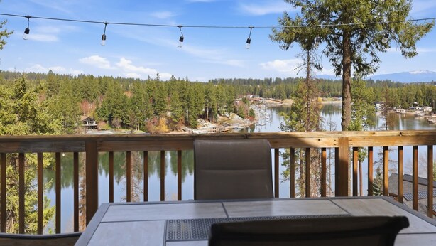 Eine Holzterrasse mit Tisch und Stühlen mit Blick auf einen See mit Booten, umgeben von Bäumen und einem klaren Himmel.